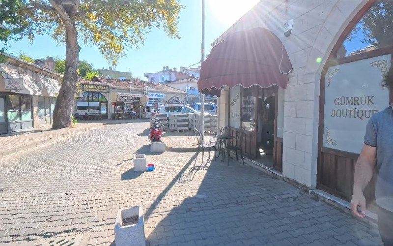 Gümrük Boutique dükkânının sokaktan görünüşü: bordo tenteli giriş, taş kemerli cephe ve vitrindeki işletme adı